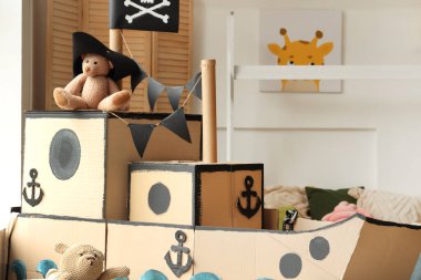 Çocuk odasındaki karton gemide korsan şapkalı oyuncak ayı.
