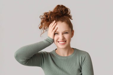 Kahverengi arka planda yüzünü kapatan utangaç genç kadın portresi.