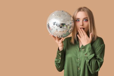 Kahverengi arka planda disko topu olan güzel, şok olmuş genç bir kadın.