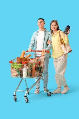 Mavi arka planda alışveriş arabası ve ödeme terminali olan genç çift.
