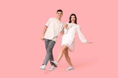 Mutlu genç çift pembe arka planda dans ediyor