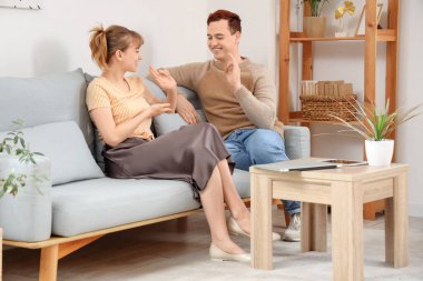 Genç sağır ve dilsiz çift evdeki kanepede işaret dili kullanıyor.