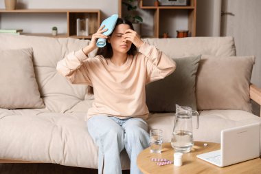 Evde ısıtma yastığıyla baş ağrısı çeken genç bir kadın.