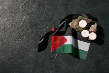 Filistin bayrağı, taşlar ve siyah arka planda yanan mumlar.