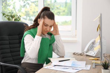Ofiste evrak işi yaparken baş ağrısı çeken genç bir kadın.
