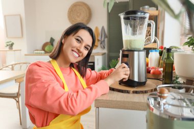 Mutfakta blenderlı genç bir kadın smoothie yapıyor.