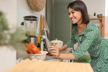 Mutfakta tablet bilgisayar kullanan blenderi olan genç bir kadın.