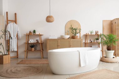 Modern banyo kozmetik ürünleri, ev bitkileri ve bornozlu.