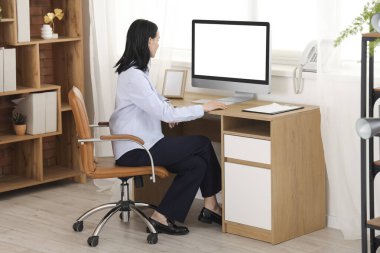 Modern ofiste bilgisayarla çalışan genç bir kadın.