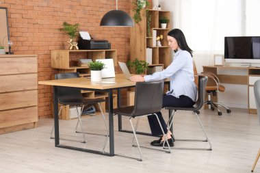 Modern ofiste dizüstü bilgisayarla çalışan genç bir kadın.