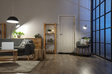 Rahat kanepesi, masası, modern dizüstü bilgisayarı ve parlayan lambaları olan bir oturma odası.