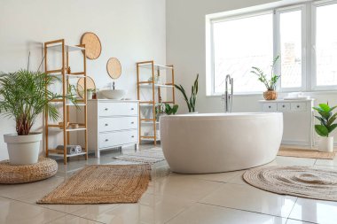Interior of light bathroom with bathtub and houseplants