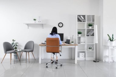 İş yerinde çalışan genç bir kadın modern bilgisayar ve dizüstü bilgisayarla aydınlık ofiste çalışıyor.