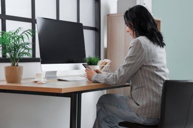 İş yerinde cep telefonu kullanan genç bir kadın modern bilgisayarla güzel bir ofiste.