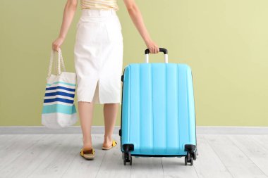 Yeşil arka planda bavulu ve çizgili çantası olan genç bir kadın. Arka plan