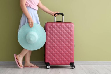 Yeşil arka planda bavulu ve şapkası olan genç bir kadın.