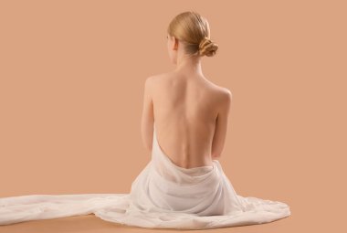 Kumaşlı ve arkası çıplak, kahverengi arka planda oturan güzel genç bir kadın.