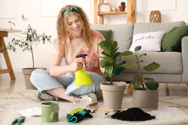 Evde yeşil bitkiyle ilgilenen genç bir kadın.