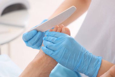 Genç adam spa salonundaki kanepede dosyasıyla profesyonel pedikür yaptırıyor.