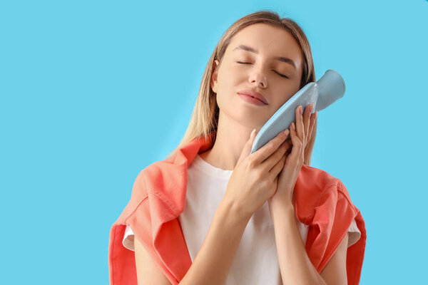 Молодая женщина с бутылкой горячей воды чувствует облегчение от зубной боли на синем фоне