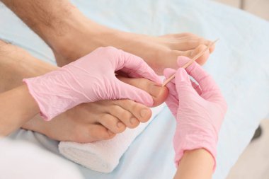Genç adam kaplıca salonundaki kanepede tahta çubukla profesyonel pedikür yaptırıyor.