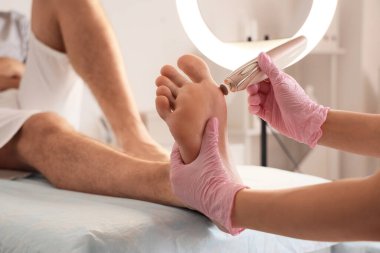 Beautician peeling feet of young man on couch in spa salon, closeup clipart