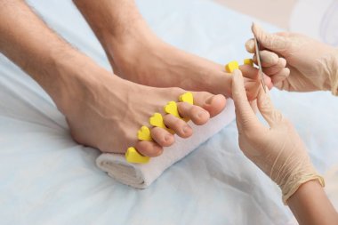 Genç adam ayak parmağı ayırıcı ile profesyonel pedikür yaptırıyor ve kaplıca salonundaki kanepeye yerleştiriliyor.