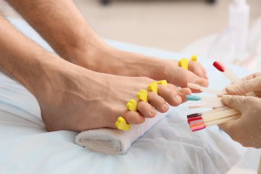 Genç adam, kaplıca salonundaki kanepede tırnak törpüsü ve ojeli profesyonel pedikür yaptırıyor.