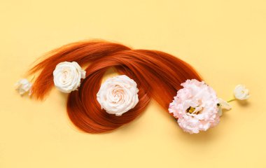 Kızıl saç teli ve soluk sarı arka planda çiçekler, yakın plan.