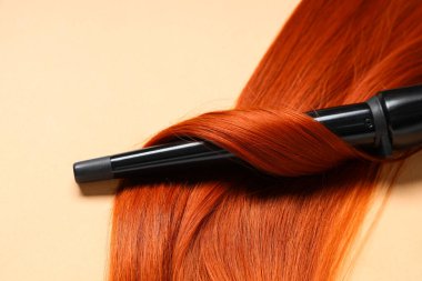 Bej arka planda kızıl saçlı saç maşası, yakın plan.