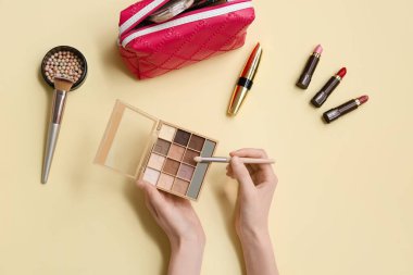 Göz falı paleti olan kadın elleri ve renk arkaplanı üzerinde farklı kozmetik ürünleri