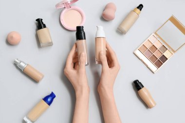 Gri arkaplanda makyaj malzemesi şişeleri olan kadın elleri, yakın plan.