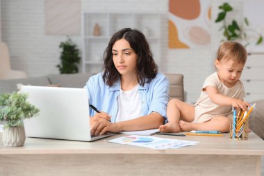 Evde doğum iznini not ederken dizüstü bilgisayarla çalışan sevimli küçük bebek ve genç anne.