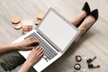 Kozmetik ürünleriyle makyaj sanatçısı ahşap zeminde dizüstü bilgisayar kullanıyor, yakın plan.