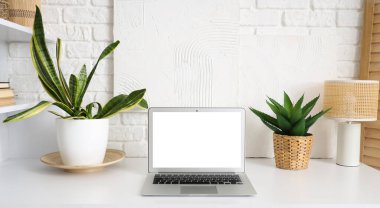 Modern dizüstü bilgisayarı olan bir işyeri ve beyaz tuğla duvarın yanındaki bitkiler.