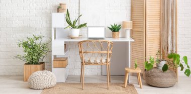 Modern dizüstü bilgisayarı olan bir işyeri ve beyaz tuğla duvarın yanındaki bitkiler.