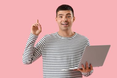 Dizüstü bilgisayarı olan genç bir adam ve pembe arka planda işaret parmağı kaldırmış.