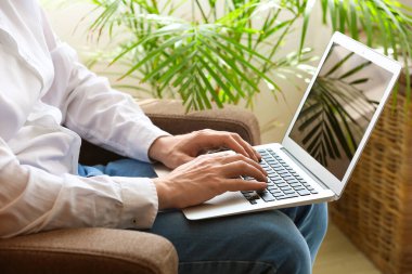 Dizüstü bilgisayarı olan adam koltukta oturuyor.