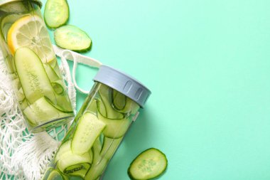 Turkuaz arka planda salatalık dilimli spor şişeleri.