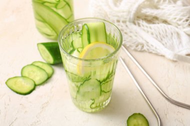 Beyaz masa üzerinde salatalık dilimleri ile doldurulmuş bardak ve bir şişe su.