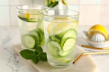 Beyaz masa üzerinde salatalık dilimleri ve eritilmiş su bardakları