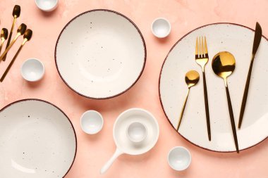 Temiz tabak, kase ve pembe masadaki altın çatal bıçak takımı.