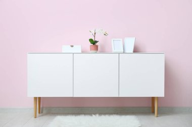 Orkide çiçekli beyaz çekmece ve odada pembe duvarın yanında boş resimler.