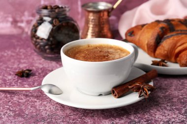 Kahve çekirdekli bir fincan nefis espresso ve mor arka planda kruvasan, yakın plan.