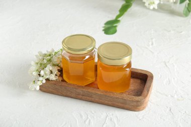 Arkaplanda akasya çiçekleri olan bal kavanozları