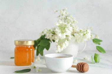 Hafif arka planda akasya çiçekleri olan bal kasesi ve kavanoz, yakın plan.