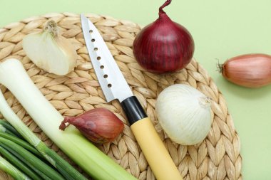 Yeşil arka planda farklı soğan türleri olan hasır paspas, yakın plan.