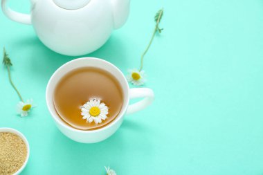 Çaydanlık ve bir fincan turkuaz arka planda sıcak papatya çayı.