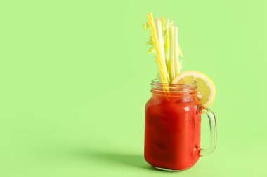 Yeşil zemin üzerinde kereviz ve limon olan bir kavanoz Bloody Mary.