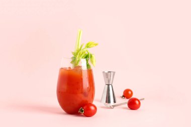 Bir bardak Bloody Mary, kereviz ve pembe arka planda domatesler.